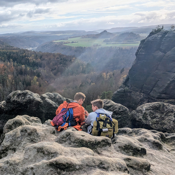 Zwei Jungen sitzen auf Berg und haben eine weite Aussicht