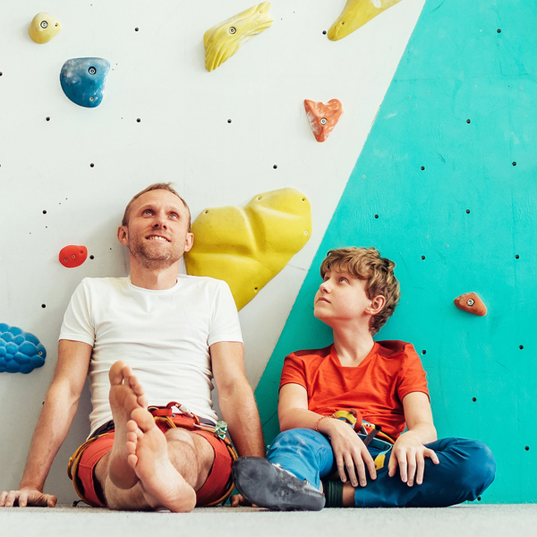 Ein Mann und ein Kind sitzen vor einer Kletterwand